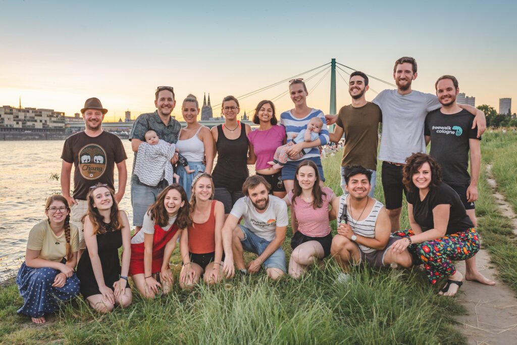 Un grupo de guias de free tour miran a la cámara. En el fondo está la Catedral de Colonia, el río Rin y un puente.