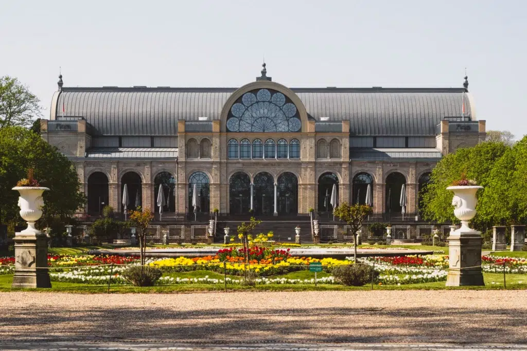 Cologne's Botanical Garden A large building sits in the background of a Parisian-styled full of flowers on a sunny day.