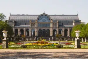 A large building sits in the background of a Parisian-styled full of flowers on a sunny day.